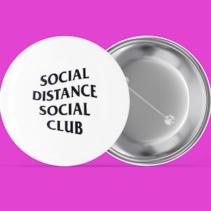 Peut inclure: Un bouton blanc avec un dos argenté. Le bouton porte le texte "SOCIAL DISTANCE SOCIAL CLUB" en noir.