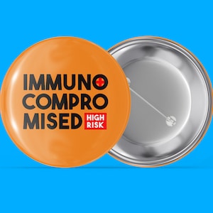Könnte beinhalten: Orangener Knopf mit dem Text "Immunsupprimiert Hohes Risiko" in schwarzen Buchstaben mit einem roten Pluszeichen. Die Rückseite des Knopfes ist silber.