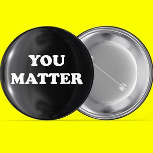 Könnte beinhalten: Ein schwarzer Knopf mit silberner Rückseite trägt die Aufschrift "YOU MATTER" in weißen Buchstaben.