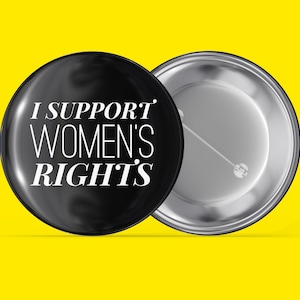 Pode incluir: Botão preto com texto branco que diz "I SUPPORT WOMEN'S RIGHTS". A parte de trás do botão é prateada.