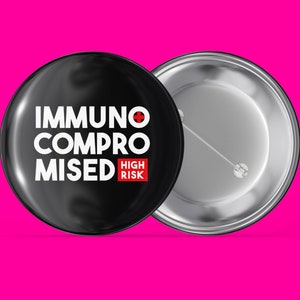 Könnte beinhalten: Schwarzer Knopf mit weißem Text, der "Immunsupprimiert Hohes Risiko" mit einem roten Pluszeichen lautet. Die Rückseite des Knopfes ist silber.