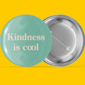 May include: A teal blue button with a white pin back. The front of the button has the text "Kindness is cool" in a white font.
