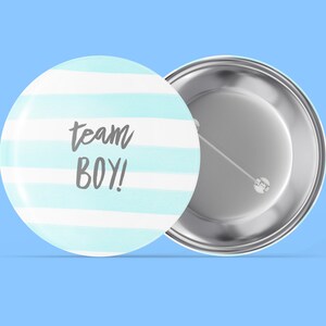 Può includere: Un bottone rotondo con un design a strisce blu e bianche. Il bottone ha il testo "team BOY!" scritto in grigio. Il retro del bottone è argentato.
