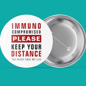 May include: White button with the text "Immunocompromised Please Keep Your Distance You Might Save My Life" in black and red lettering. The back of the button is silver.