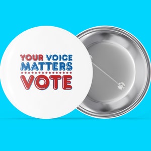 May include: White badge with the text "YOUR VOICE MATTERS VOTE" in red and blue. The badge has a pin back and is displayed on a bright blue background. The text is surrounded by stars.