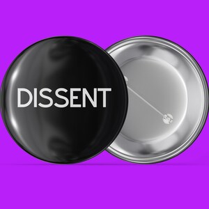 May include: A black button with a silver back. The button has the word "DISSENT" printed in white on the front.