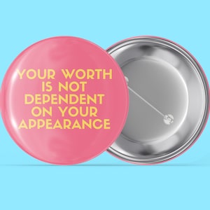 Può includere: Bottone rosa con una scritta gialla che dice "YOUR WORTH IS NOT DEPENDENT ON YOUR APPEARANCE".