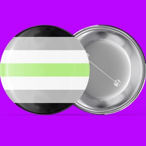 May include: A round button with a black, white and light green striped design. The back of the button is silver with a pin.