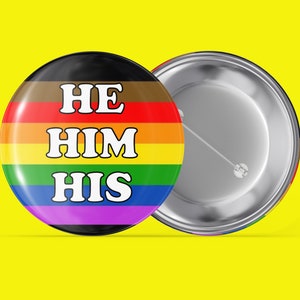 May include: A rainbow pride flag button with the text "HE HIM HIS" in white letters.