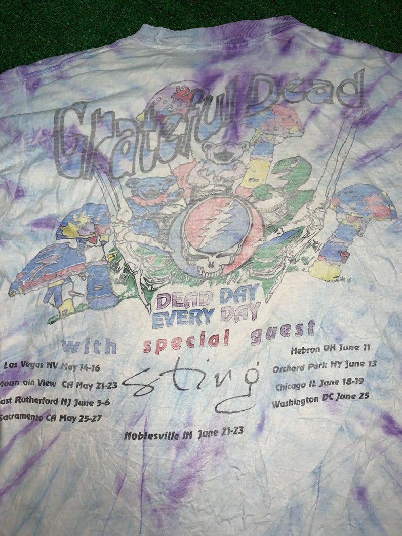 以下が含まれることがあります： タイダイ染めのTシャツに、グレイトフル・デッドのグラフィックと「Dead Day Every Day」の文字、そして「special guest Sting」の文字がプリントされています。Tシャツには、5月と6月のバンドのツアーの日程が記載されています。