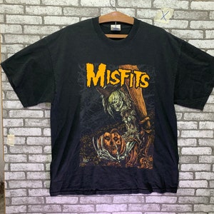 May include: Black t-shirt with a graphic print of a spooky figure holding a jack-o'-lantern. The text "Misfits" is printed in yellow letters on the shirt.