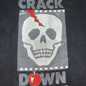 May include: Black t-shirt with a graphic print of a cracked skull with a red crack and the words "CRACK DOWN" with a red apple.