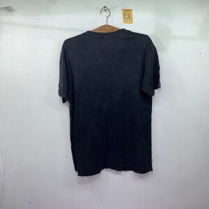 May include: A black short-sleeved t-shirt hanging on a hanger against a white wall.