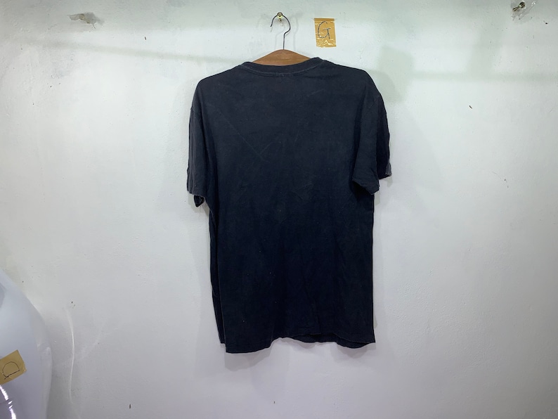 May include: A black short-sleeved t-shirt hanging on a hanger against a white wall.