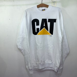 Pu&ograve; includere: Felpa bianca a maniche lunghe con un logo CAT nero e giallo. Il logo &egrave; un carattere grande e in grassetto con un triangolo giallo al centro.