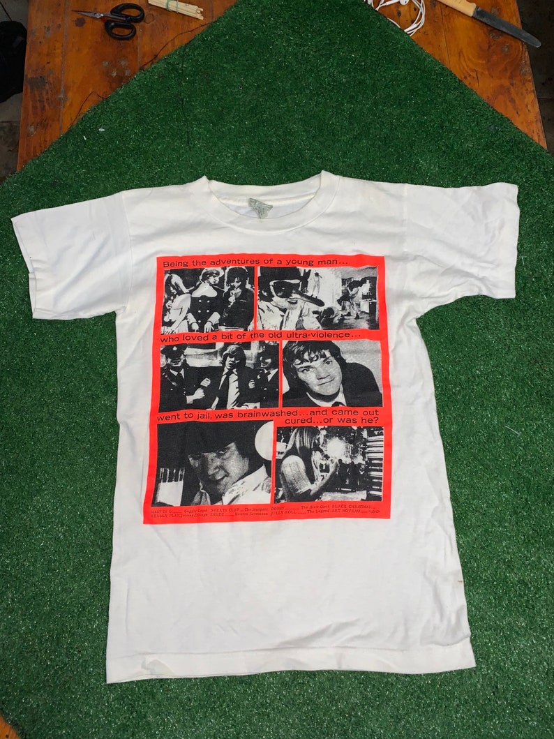 May include: White t-shirt with a red graphic print of a comic book style illustration. The text on the graphic reads "Being the adventures of a young man... who loved a bit of the old ultra-violence. went to jail, was brainwashed...and came out cured...or was he?"