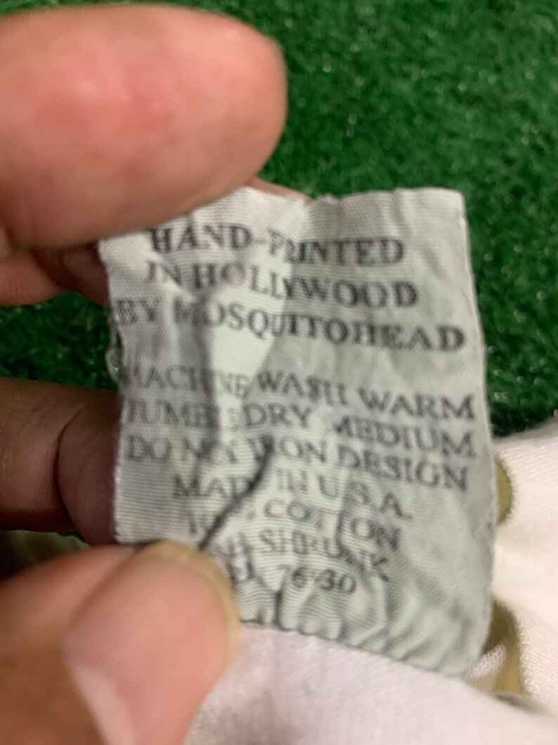 May include: White tag with black text that reads "HAND-PRINTED IN HOLLYWOOD BY MOSQUITOREAD MACHINE WASH WARM TUMBLE DRY MEDIUM DO NOT IRON DESIGN MADE IN USA COTTON SIZE UNK 7630"