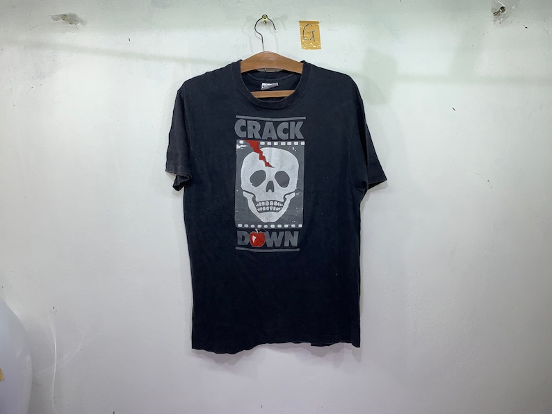 May include: Black t-shirt with a white skull graphic and the text "CRACK DOWN" printed on the front.