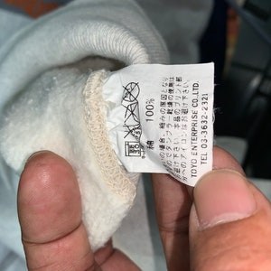May include: White cotton sweatshirt with a label that reads "100% Cotton" and "TOYO ENTERPRISE CO.,LTD. TEL 03-3632-2321".