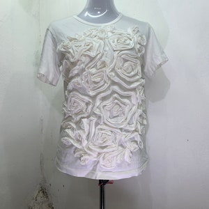 Pu&ograve; includere: Maglietta bianca a maniche corte con un grande design floreale 3D in tessuto bianco.