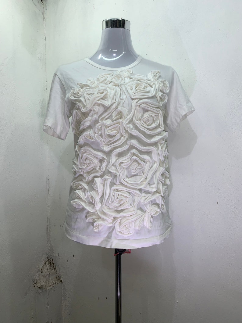 Pu&ograve; includere: Maglietta bianca a maniche corte con un grande design floreale 3D in tessuto bianco.