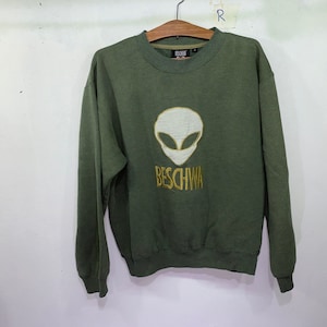 May include: Green sweatshirt with a white alien head and gold embroidery that reads "BESCHWA".