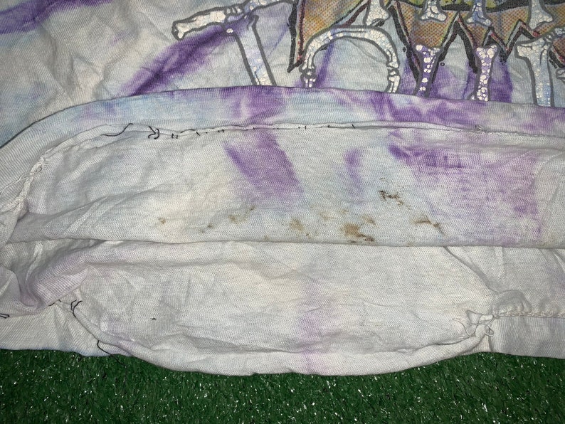 以下が含まれることがあります： 白地に紫と青のぼかし染めが施されたTシャツ。くたびれたような風合いがあり、柔らかく着心地の良い生地で作られています。