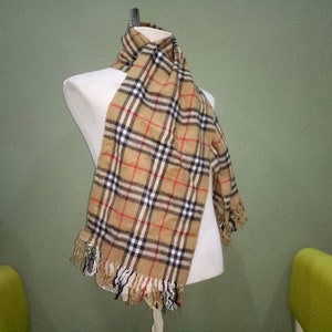 May include: A brown and beige plaid scarf with black and red accents. The scarf has fringe on the ends.