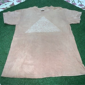 May include: A light brown t-shirt with a white triangle design. The triangle is filled with a pattern of small white shapes.