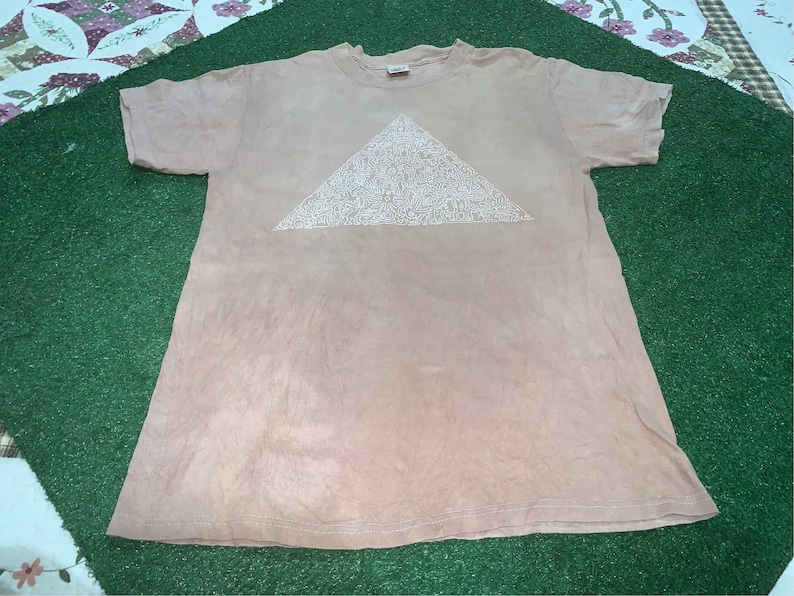 May include: A light brown t-shirt with a white triangle design. The triangle is filled with a pattern of small white shapes.