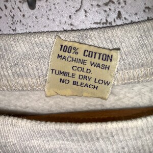 May include: A white cotton sweatshirt tag with the text "100% COTTON MACHINE WASH COLD. TUMBLE DRY LOW NO BLEACH."