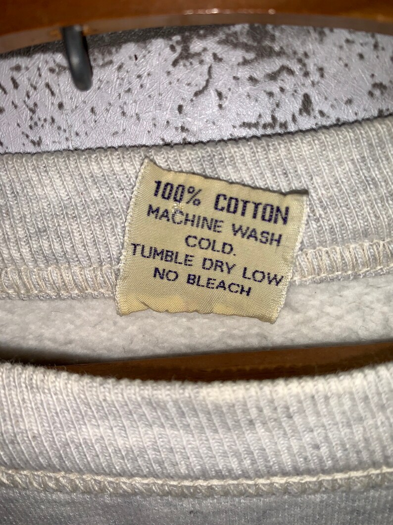 May include: A white cotton sweatshirt tag with the text "100% COTTON MACHINE WASH COLD. TUMBLE DRY LOW NO BLEACH."