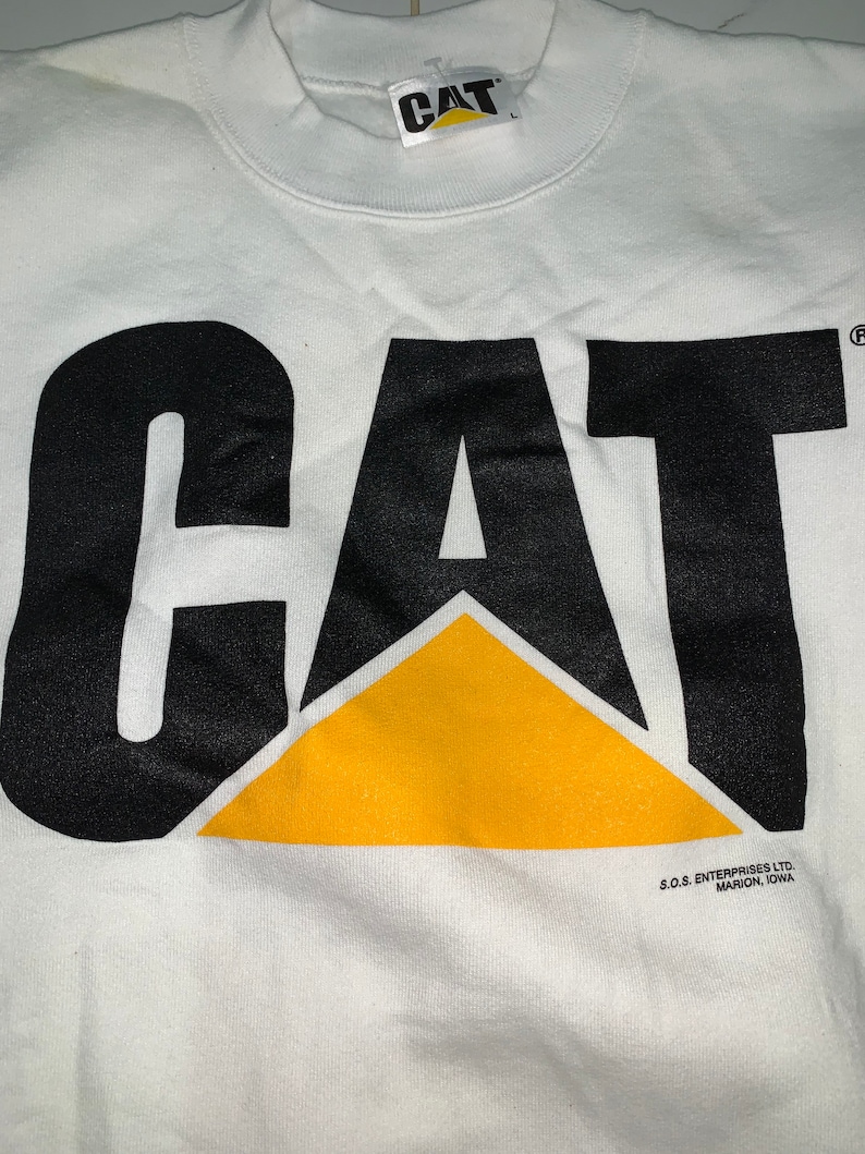Pu&ograve; includere: Felpa bianca con un logo "CAT" nero con un triangolo giallo. Il logo &egrave; stampato sul davanti della felpa. La felpa ha un collo rotondo e maniche lunghe. Il testo "S.O.S. ENTERPRISES LTD. MARION, IOWA" &egrave; stampato sul fondo della felpa.