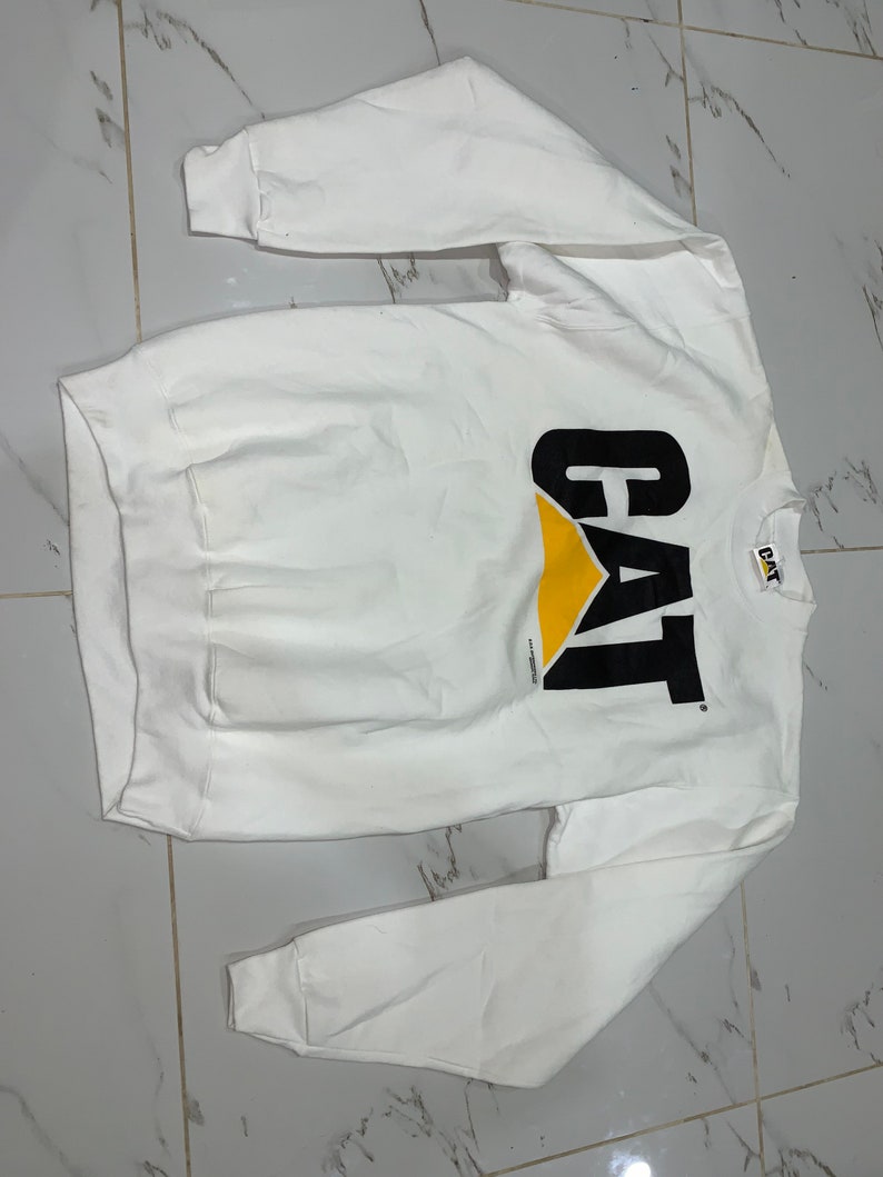 Pu&ograve; includere: Felpa bianca a maniche lunghe con logo CAT nero e giallo.