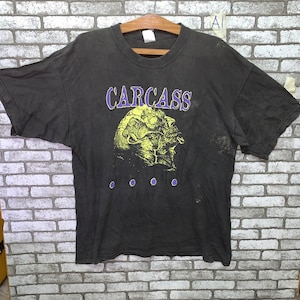 May include: Black t-shirt with a yellow and purple graphic of a skull and the word "CARCASS" printed on the front.