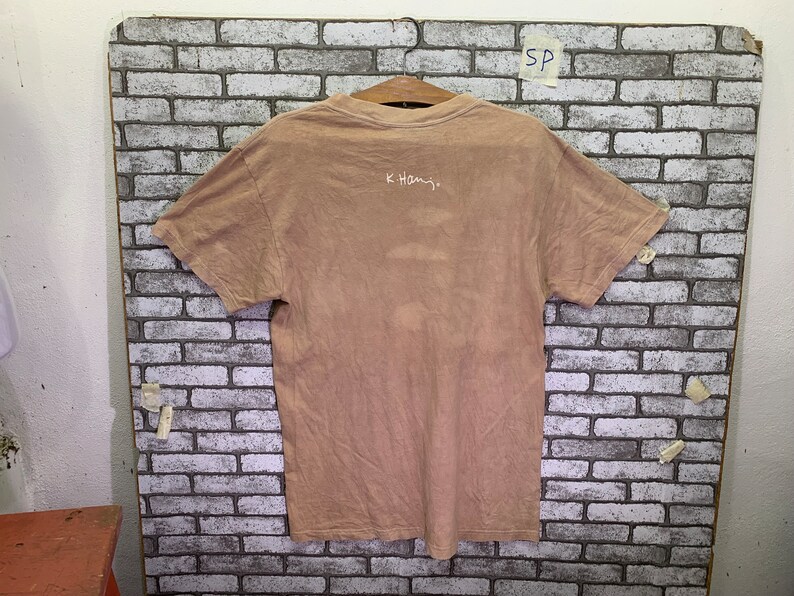 May include: A light brown t-shirt with a white inscription that reads "K.Hamj."