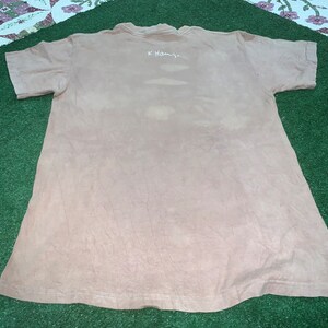 May include: A light brown t-shirt with a white inscription that reads "K. Hamby."