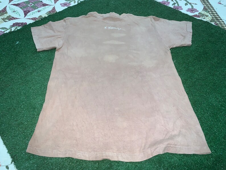 May include: A light brown t-shirt with a white inscription that reads "K. Hamby."