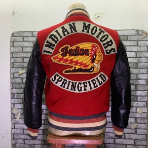 May include: Red and black varsity jacket with leather sleeves. The back features a large embroidered patch with the text "INDIAN MOTORS SPRINGFIELD" and an Indian head logo.