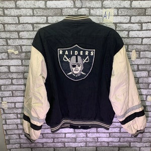 Könnte beinhalten: Schwarze und weiße Baseballjacke mit dem Oakland Raiders Logo auf der Rückseite. Das Logo zeigt einen Totenkopf mit gekreuzten Schwertern und dem Wort "RAIDERS" darüber.