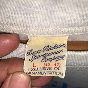 May include: A white tag with black text that reads "Buzz Rickson Sportswear Company" and "L (40-42)" with the text "EXCLUSIVE OF ORNAMENTATION" below.