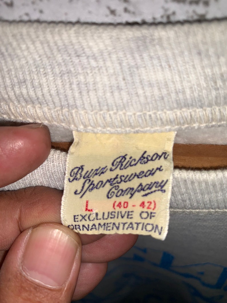 May include: A white tag with black text that reads "Buzz Rickson Sportswear Company" and "L (40-42)" with the text "EXCLUSIVE OF ORNAMENTATION" below.