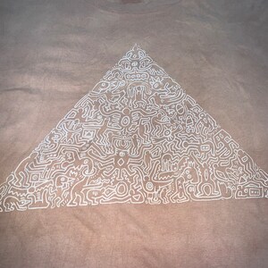 May include: A beige t-shirt with a white outline of a pyramid filled with abstract figures and symbols.