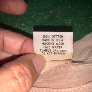 May include: A white care tag with black text that reads "100% Cotton, Made in U.S.A., Machine Wash Cold Water, Tumble Dry Low, Do Not Bleach."