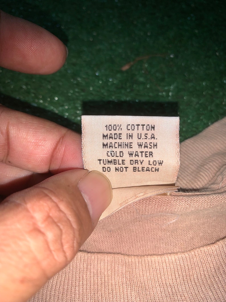 May include: A white care tag with black text that reads "100% Cotton, Made in U.S.A., Machine Wash Cold Water, Tumble Dry Low, Do Not Bleach."