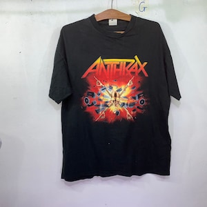 Puede incluir: Camiseta negra con un estampado gráfico de la banda Anthrax. El gráfico presenta una calavera con instrumentos musicales y altavoces en un esquema de color rojo, amarillo y negro.