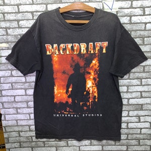 Può includere: Maglietta nera con una grafica di un pompiere in fiamme e il testo "BACKDRAFT" e "UNIVERSAL STUDIOS".