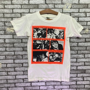May include: White t-shirt with a black and white graphic print of a band. The graphic print has the text "Being the adventures of a young man... who loved a bit of the old ultra violence went to jail, was brainwashed... and came out cured...or was he?"