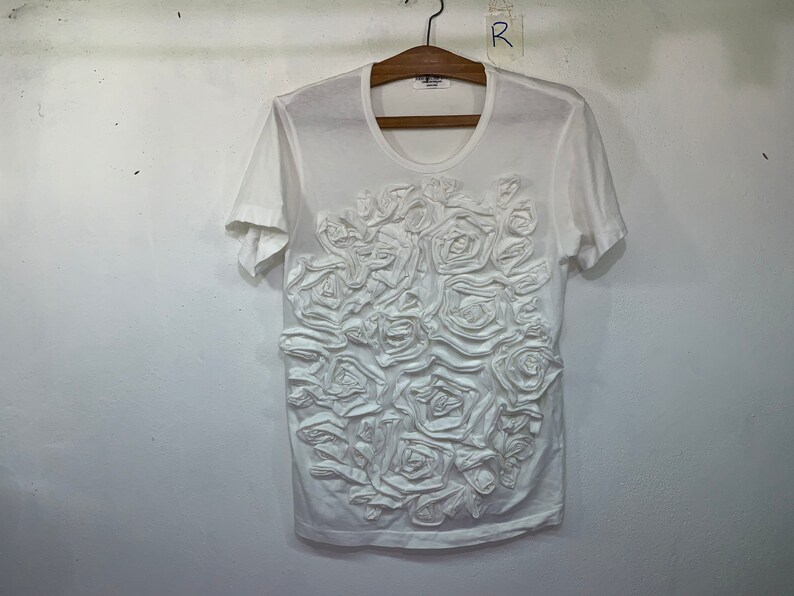 Pu&ograve; includere: Maglietta bianca a maniche corte con un design floreale 3D sul davanti.