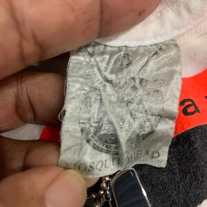 May include: Close-up of a white t-shirt with a black and white graphic print. The tag is visible and reads "Mosquit Head".
